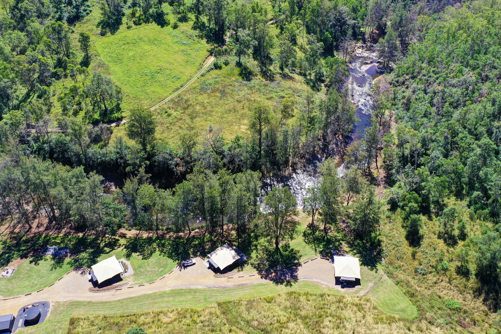 Aerial view of three riverside glamping tents along the Manning River