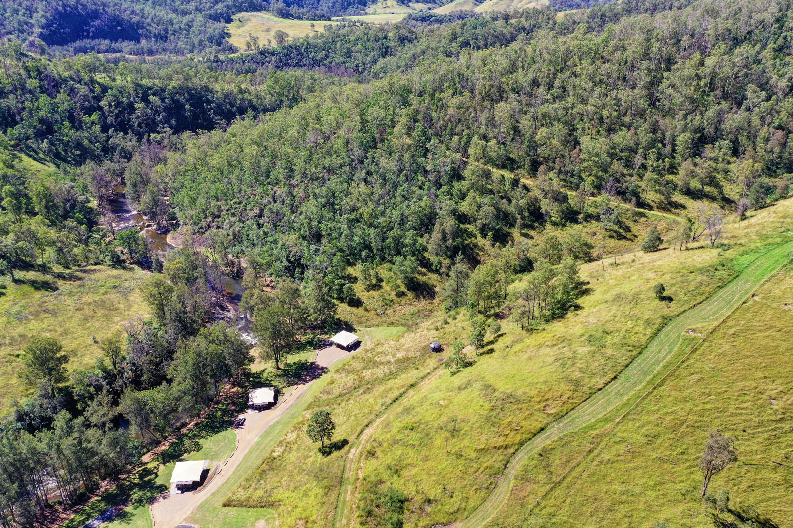 Aerial valley of bushland, river and glamping cabins at Amaroo Escape